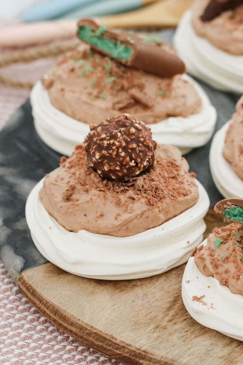 Mini pavlovas filled with a hazelnut filling and a chocolate on top, on a serving board