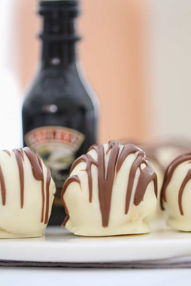 A close up of cheesecake balls, drizzled with chocolate, in front of a bottle of Baileys