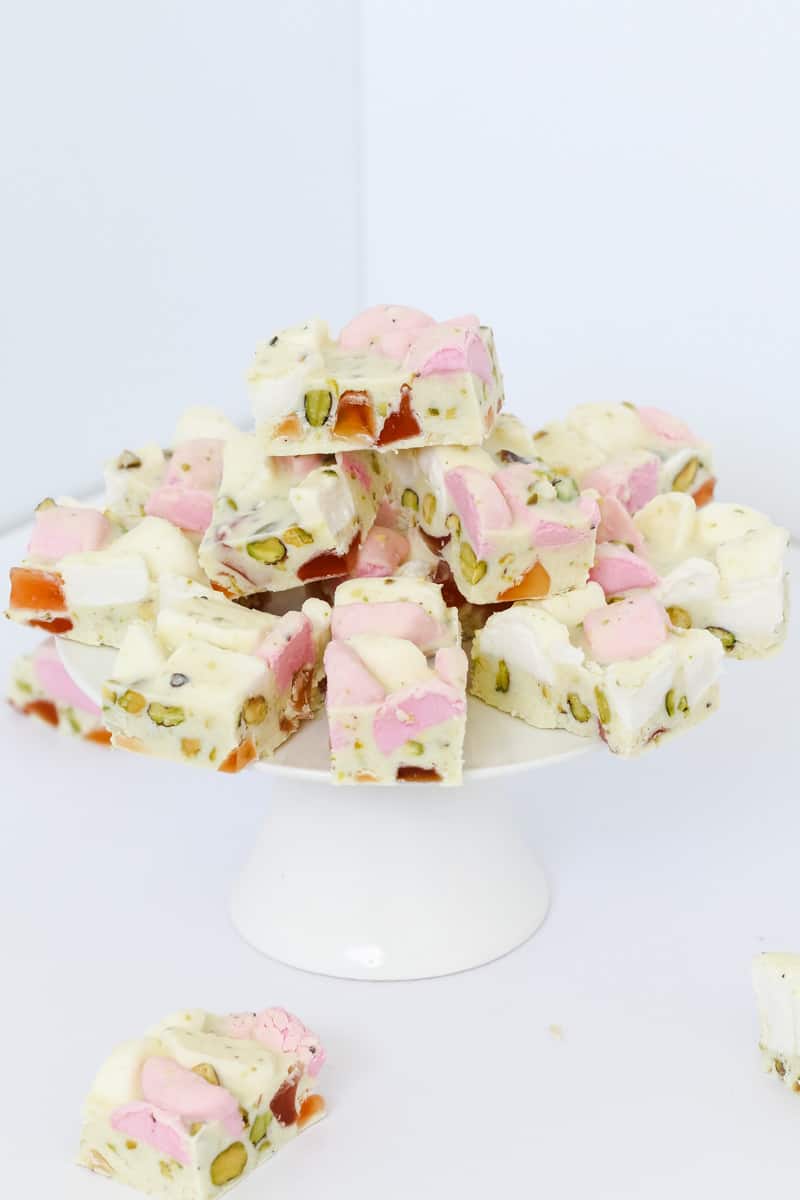 A white cake stand with a stack of white chocolate Rocky Road filled with marshmallows, turkish delight and pistachios