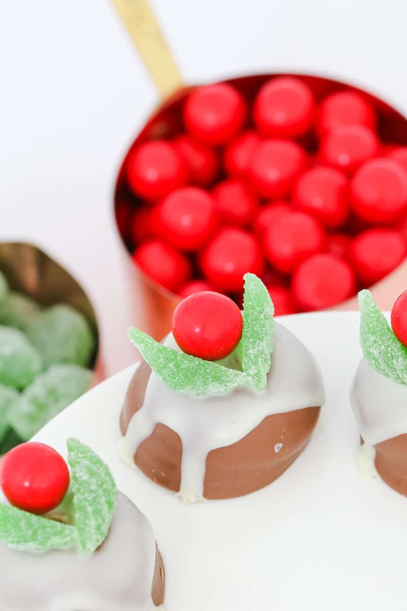 Chocolate Christmas puddings made from chocolate marshmallow biscuits, melted white chocolate, jaffas and spearmint leaves on a white plate.