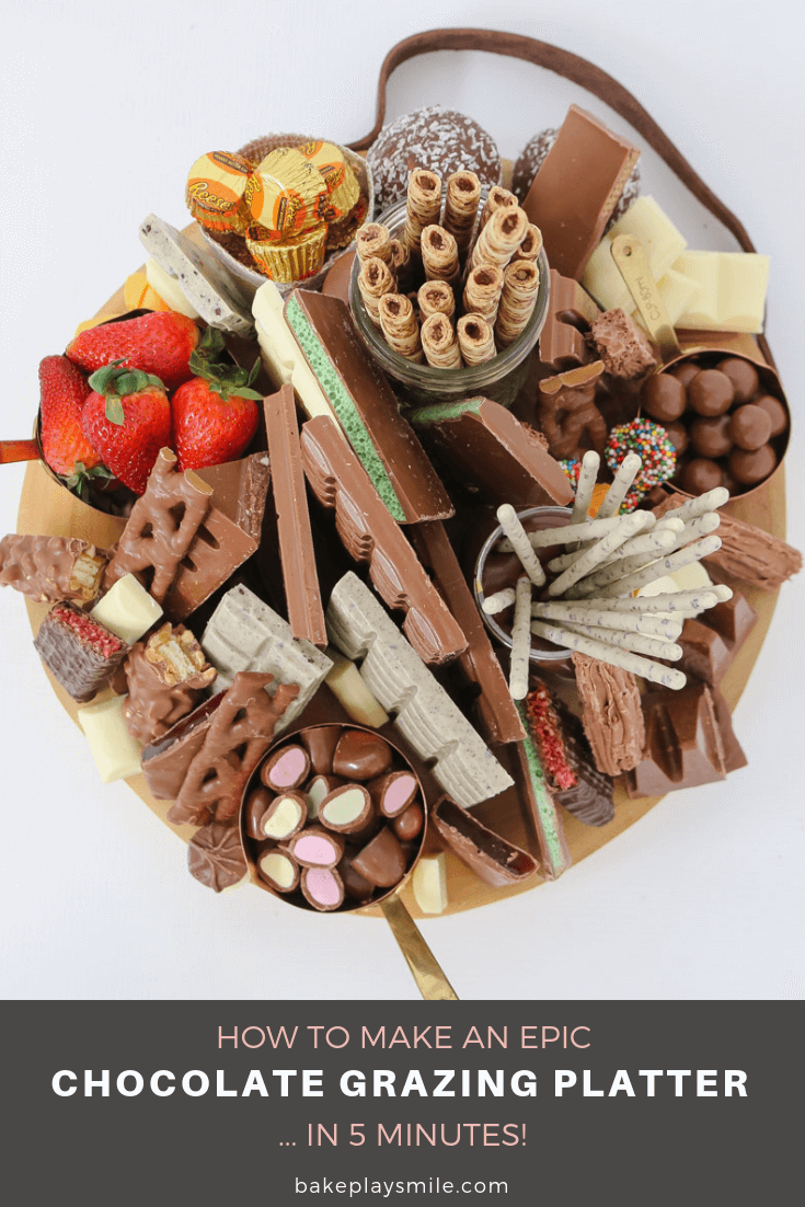 A round wooden board packed with different types of chocolate treats and strawberries.