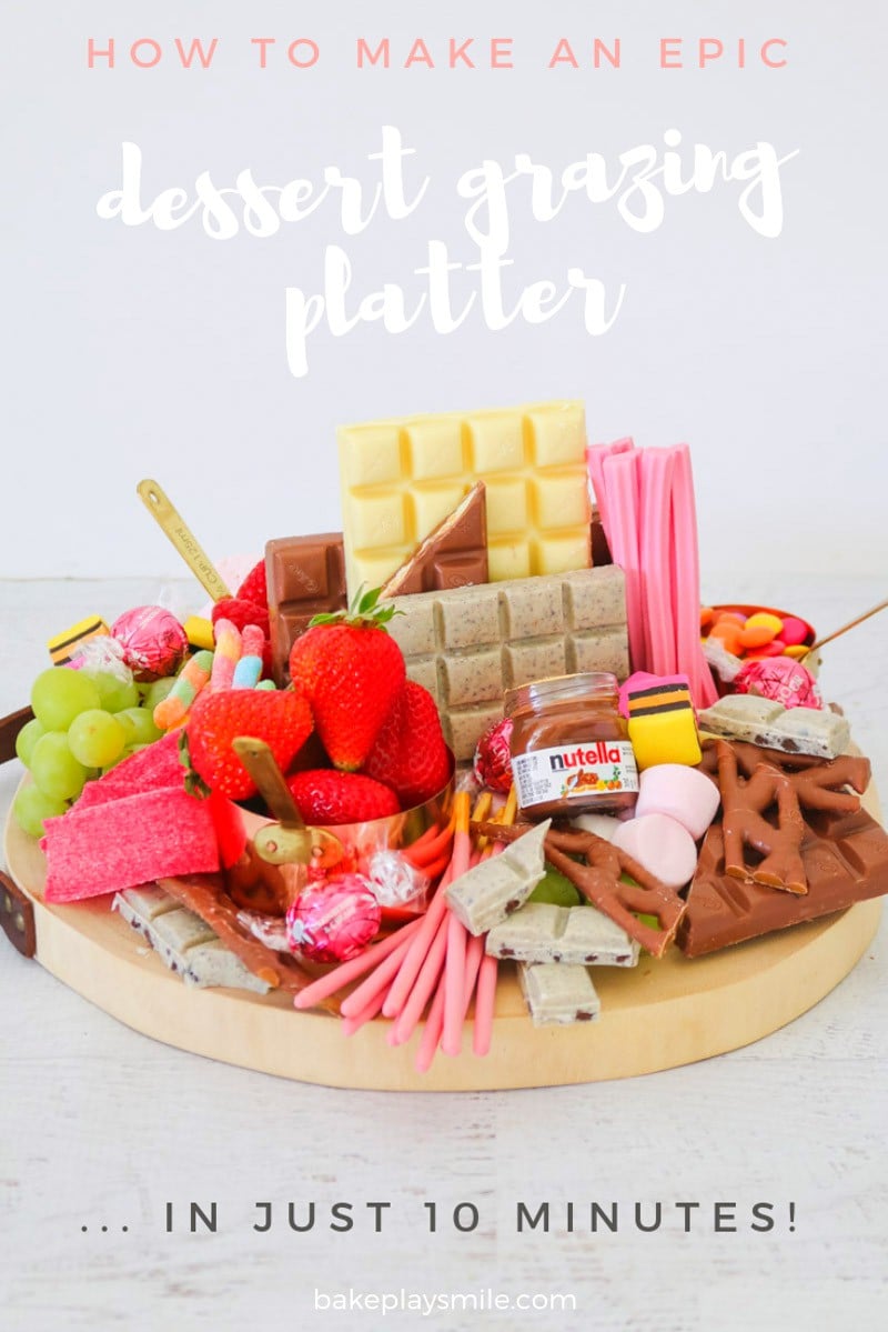 A round wooden board packed with a selection of chocolate bars, grapes, strawberries and lollies.