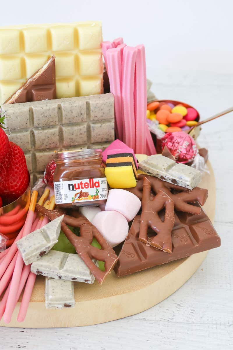 A close up of chocolate bars, a small jar of Nutella, strawberries and assorted lollies on a wooden board