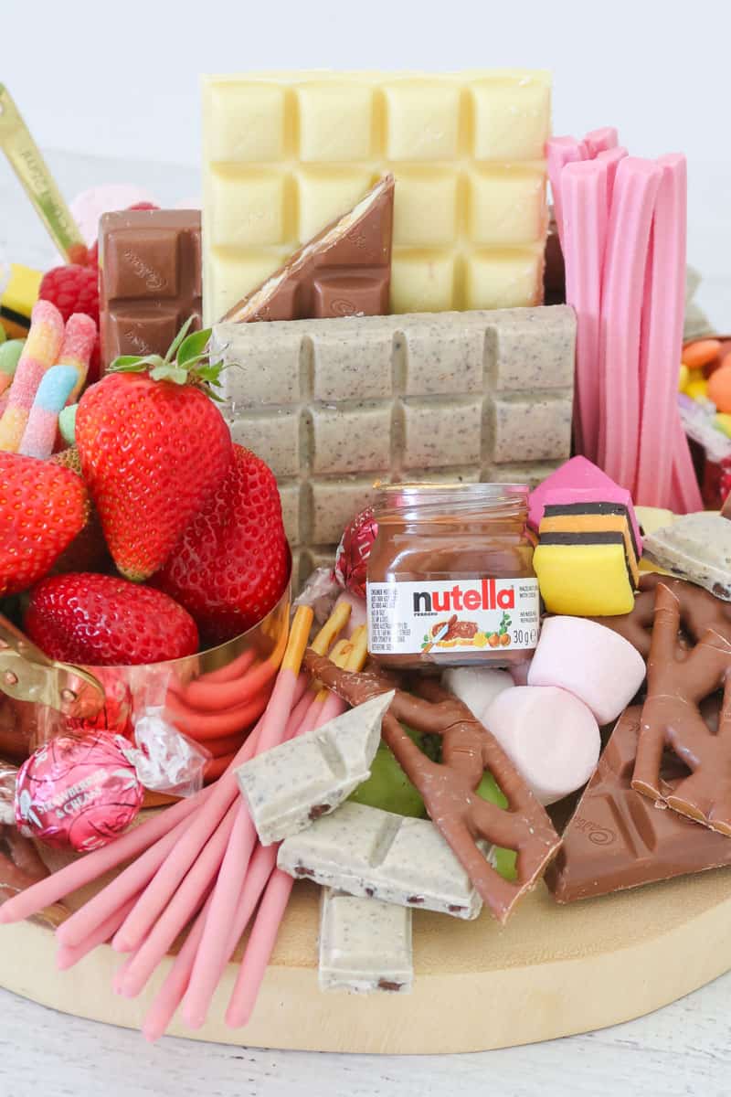 A selection of chocolate bars, a small jar of Nutella, strawberries in a copper cup, and assorted lollies.