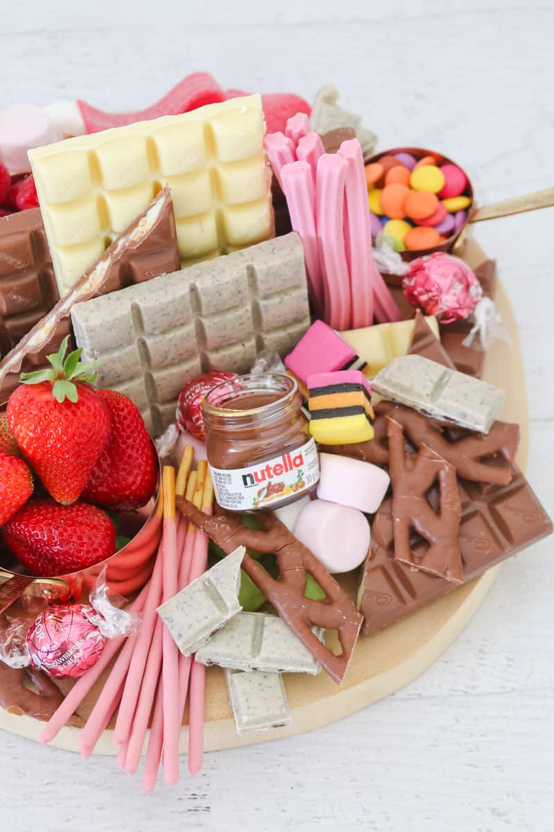 A wooden board packed with chocolate bars, strawberries, a jar of chocolate hazelnut spread and assorted lollies