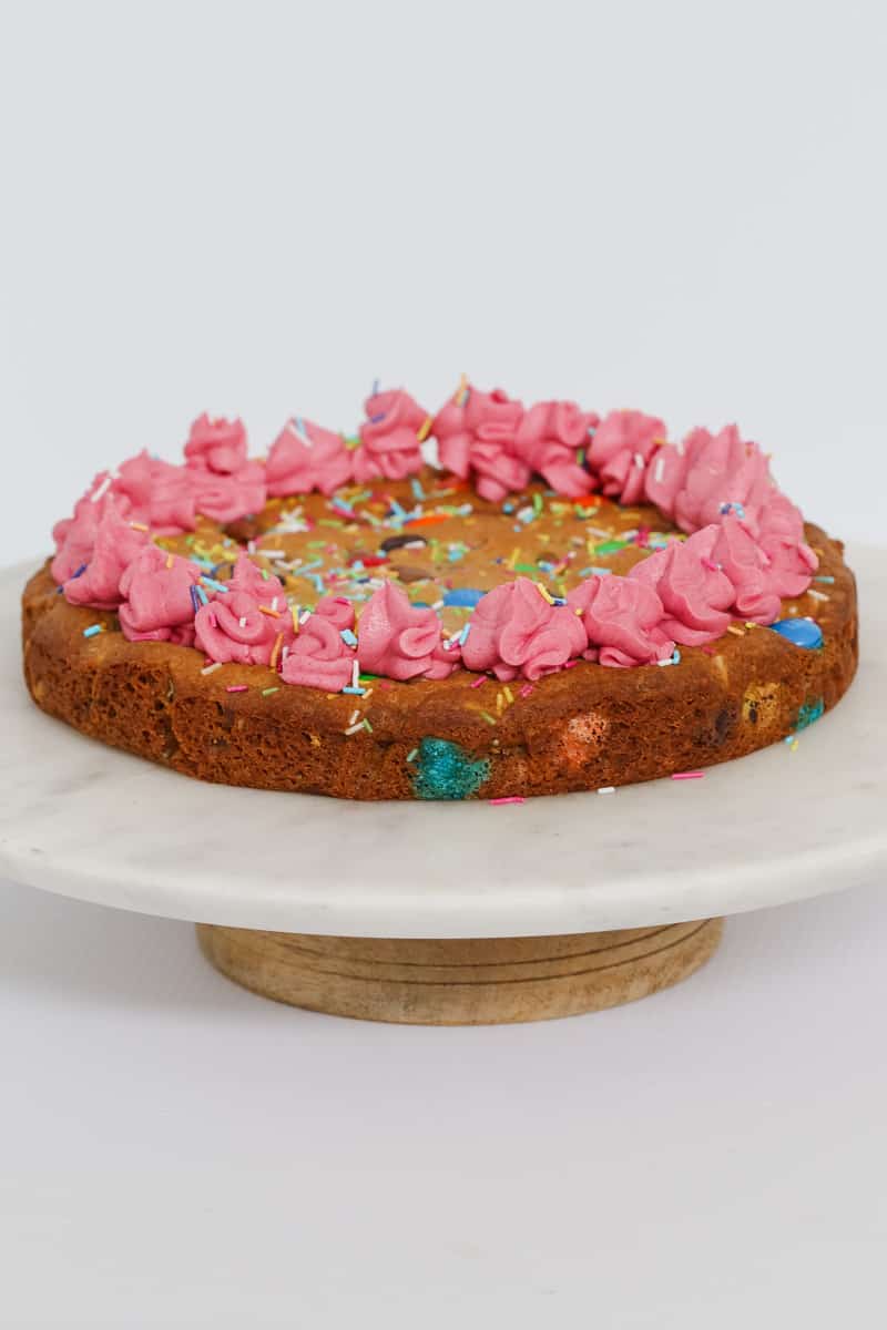 Cookie cake with pink frosting on a marble cake stand.