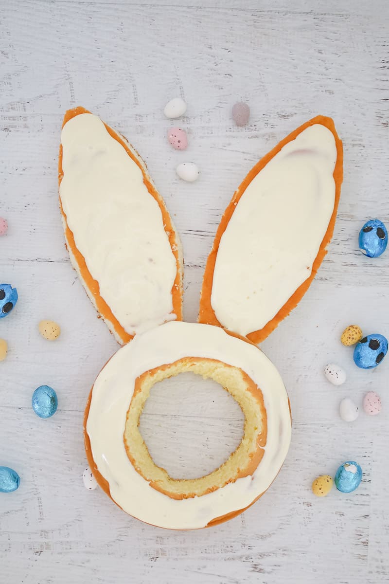 Frosting being spread over the top of sponge cakes cut into an Easter bunny shape. 