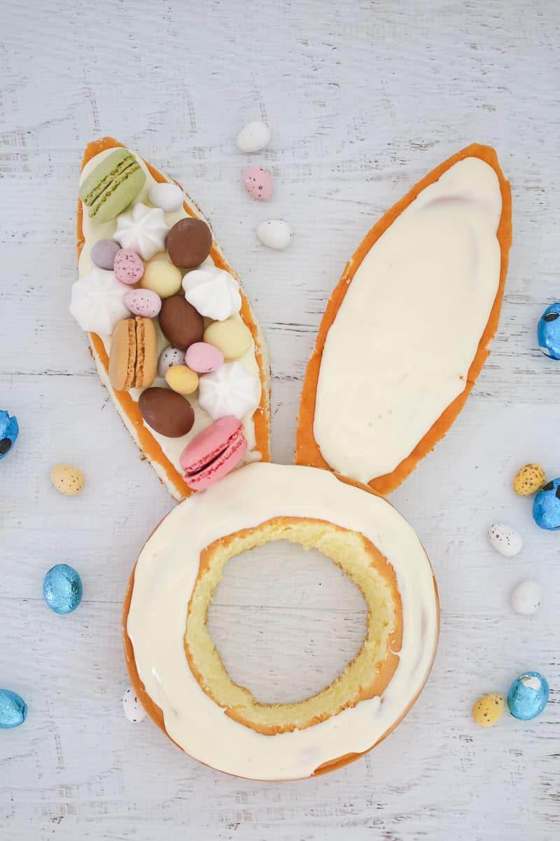 Macarons, easter eggs and mini meringues being used to decorate the ears of an Easter cake. 