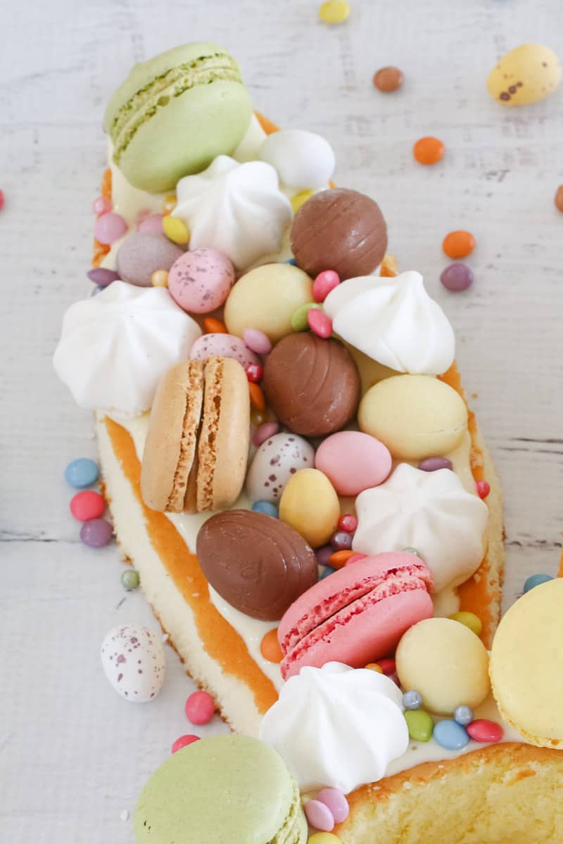 Easter eggs, French macaron cookies and meringues on top of a sponge cake cut into a bunny ear shape. 