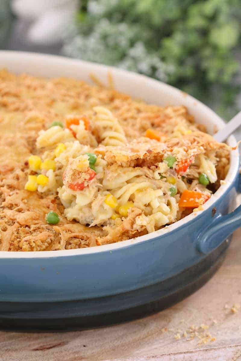 A pasta bake made with tuna, corn, peas and carrots being served from a baking dish.