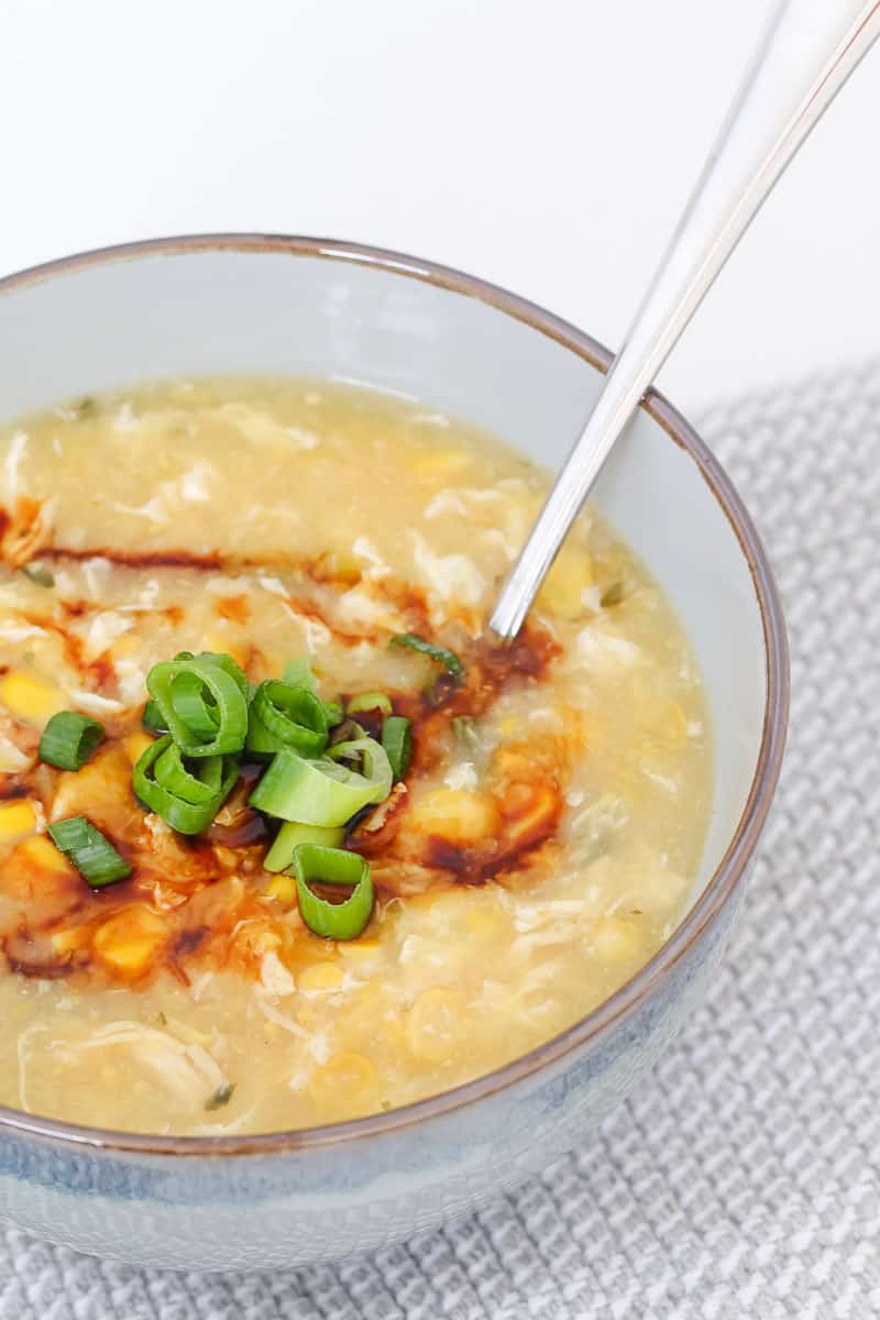 A bowl of chicken and corn soup garnished with soy sauce and spring onions.