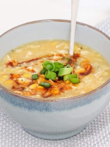 A blue bowl of Chicken and Corn soup decorated with chopped spring onions.