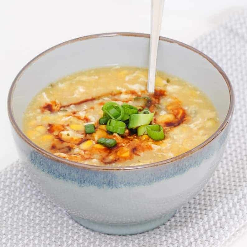 A blue bowl of Chicken and Corn soup decorated with chopped spring onions.