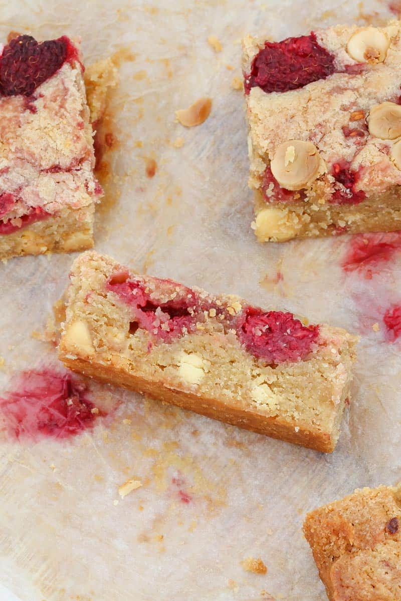 A piece of raspberry and white chocolate blondie being cut on a chopping board. 
