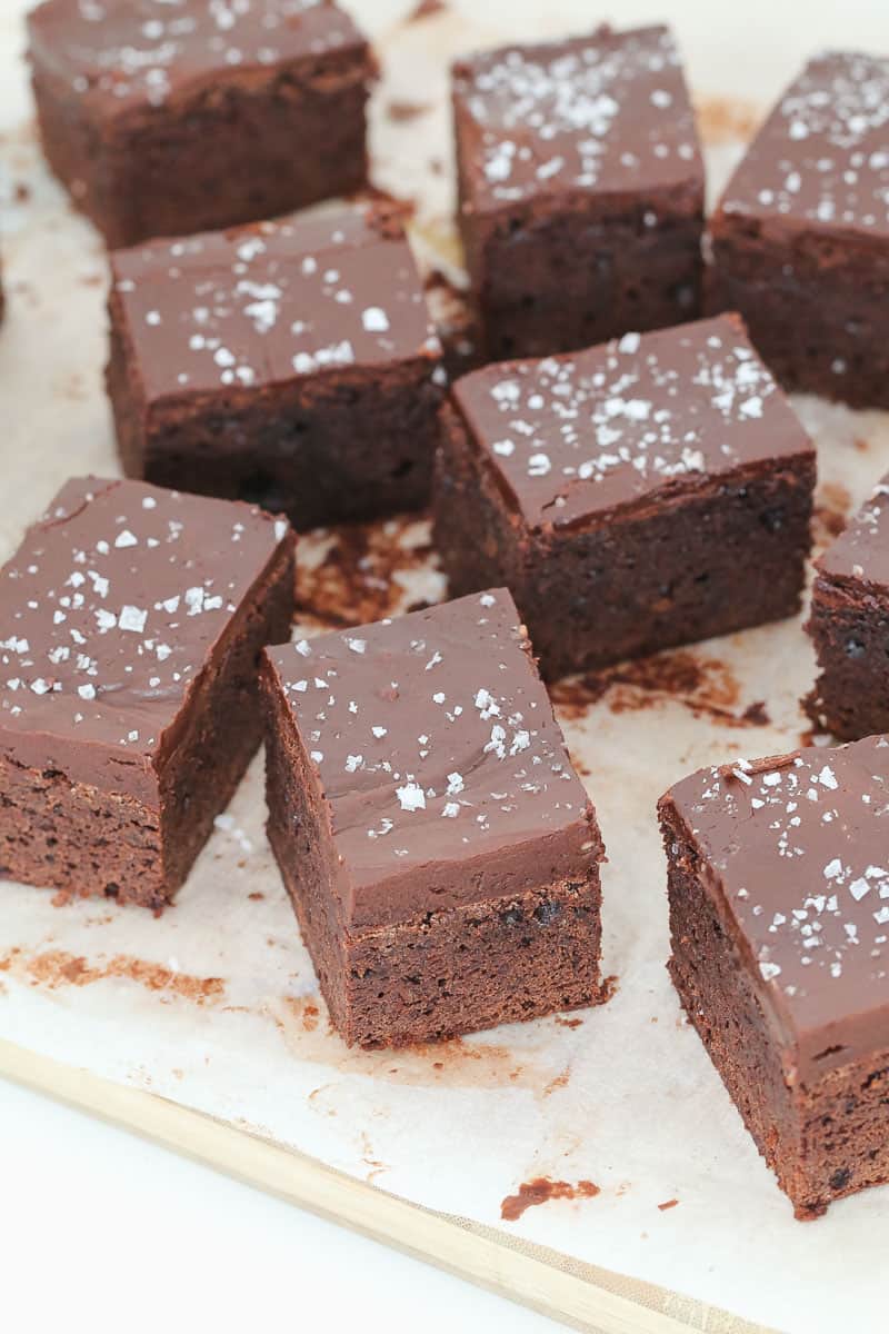 Chocolate brownies with frosting being cut up on a chopping board. 