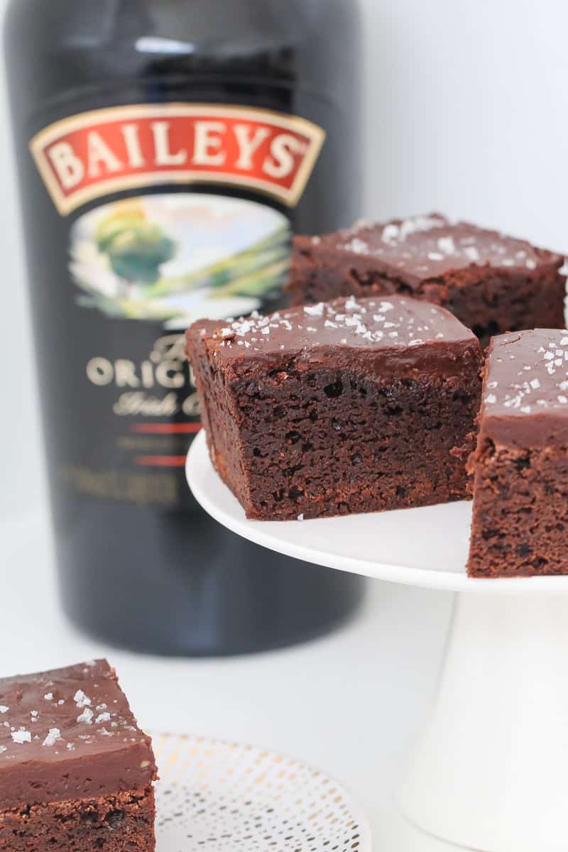 A piece of Baileys brownie on a cake plate with Irish cream in the background. 