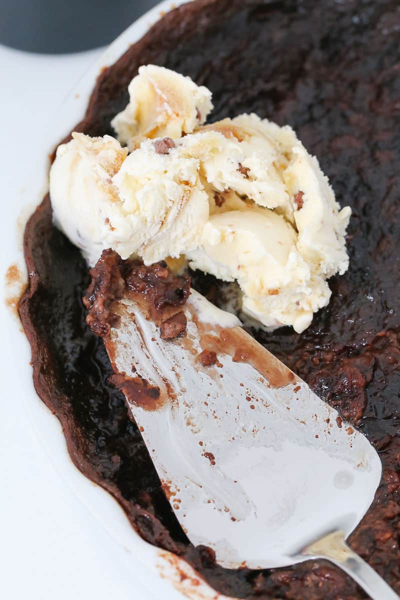 A baking dish with chocolate Baileys pudding, a cake server and a scoop of ice-cream. 