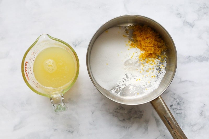 A saucepan with sugar, lemon zest and cornflour and a measuring jug filled with lemon juice.