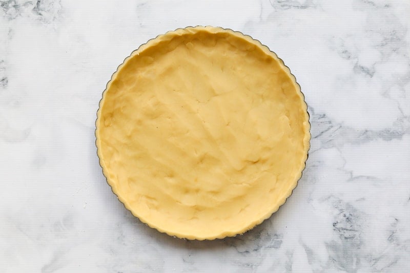 A uncooked homemade shortcrust pastry being pressed into a flan tin.