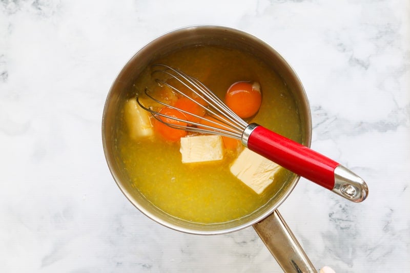 Eggs and butter being added to a saucepan with lemon.