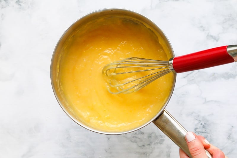 Lemon curd being stirred with a whisk in a saucepan.