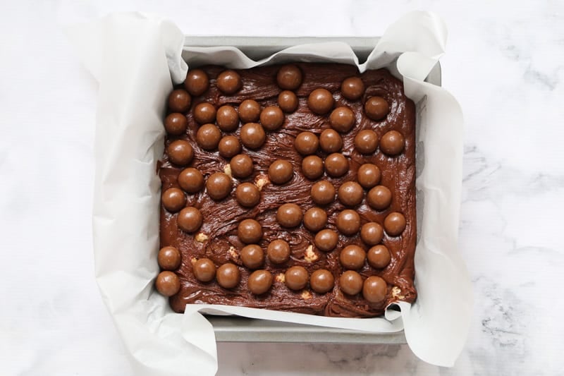 Maltesers on top of a chocolate slice in a square baking tin.