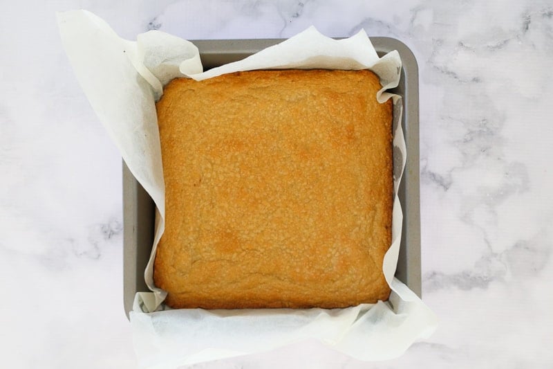 A shortbread base just out of the oven in a square baking tin.