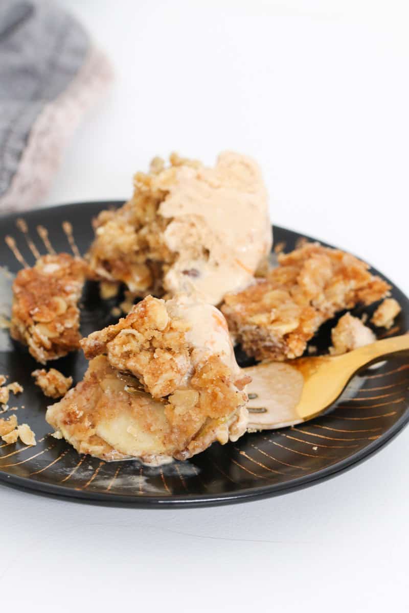 Apple crumble slice on a gold fork with ice-cream in the background. 