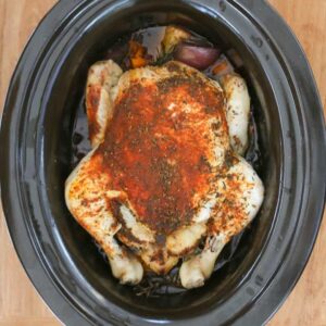 A whole chicken placed in a slow cooker with spices.