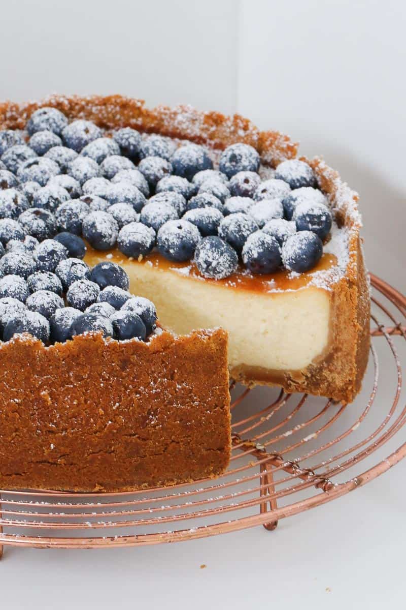 A cake plate with a baked New York cheesecake with a slice removed.