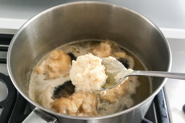 Tablespoons of golden syrup dumpling mixture going into a saucepan of simmering syrup.