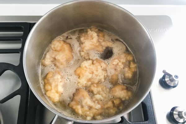 Golden syrup dumplings boiling in a saucepan of sweet syrup.