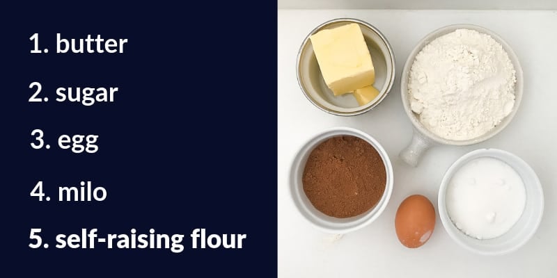 Butter, self-raising flour, caster sugar, egg and milo on a bench.