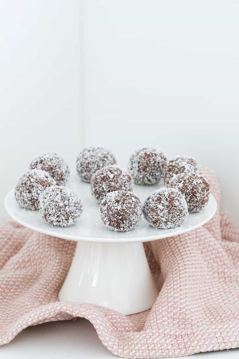 A white cake stand topped with rum balls on a pink tea towel.