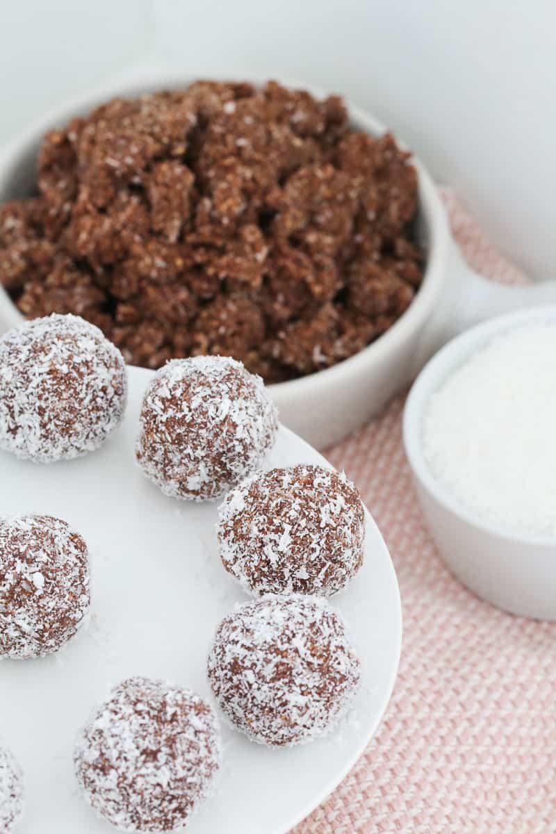 A white cake stand with rum balls on a pink tea towel in front of a bowl of mixture