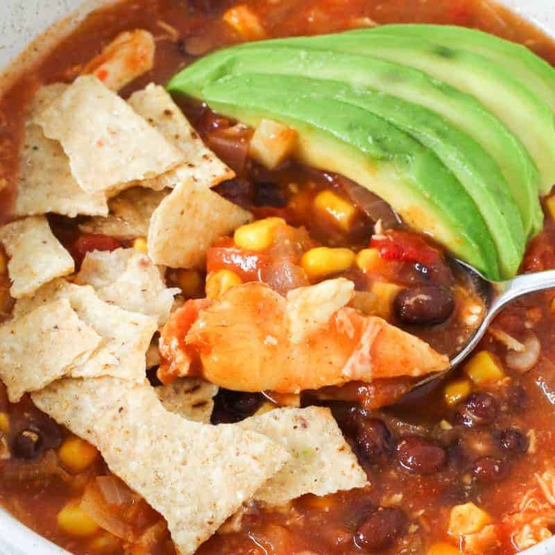 A bowl of tomato, chicken, corn and bean soup.