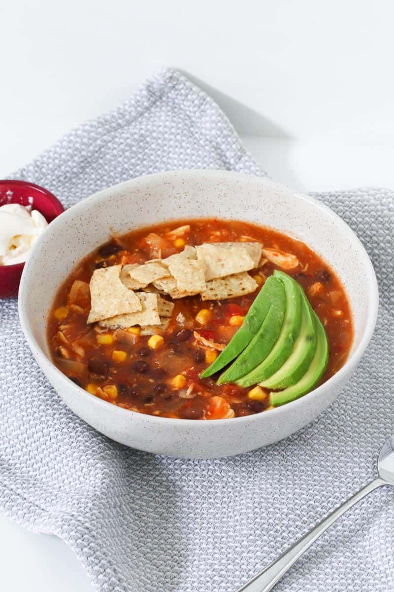 A bowl of soup with tortilla chips and avocado on top.