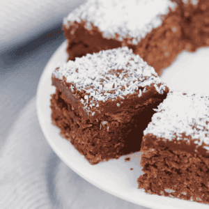Pieces of chocolate coconut slice topped with chocolate icing and sprinkled with coconut on a cake stand.