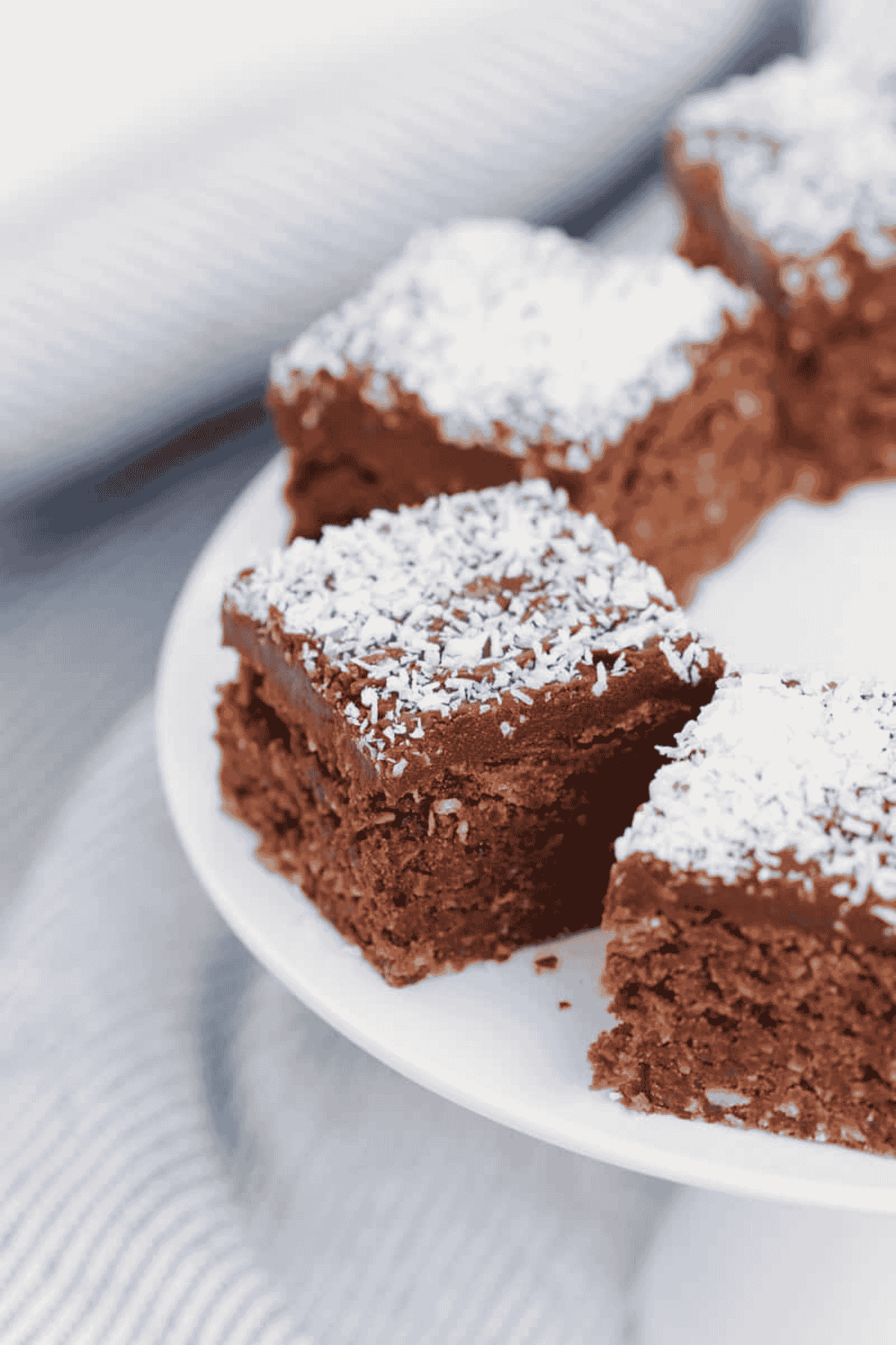 Pieces of chocolate coconut slice topped with chocolate icing and sprinkled with coconut on a cake stand.