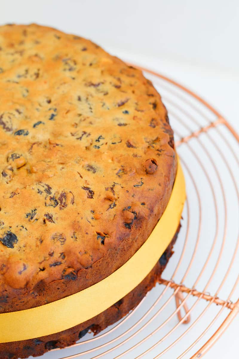 A fruit cake with a gold ribbon around it on a copper wire tray