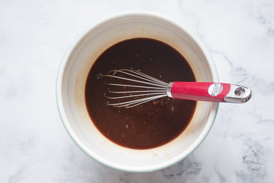 Brown sauce being whisked in a white bowl. 