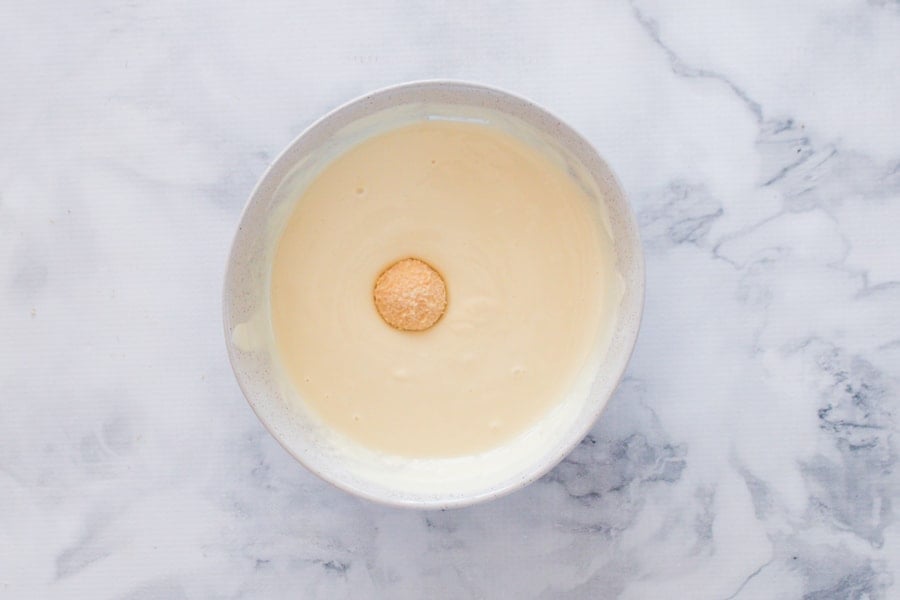 A Baileys cheesecake ball being dipped into white chocolate. 