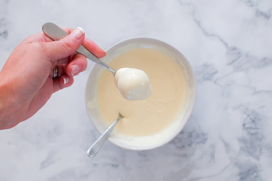 A spoon with a cheesecake ball covered in melted white chocolate. 