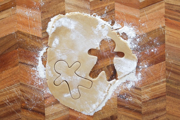 Gingerbread men shapes being cut out from dough on a lightly floured chopping board. 