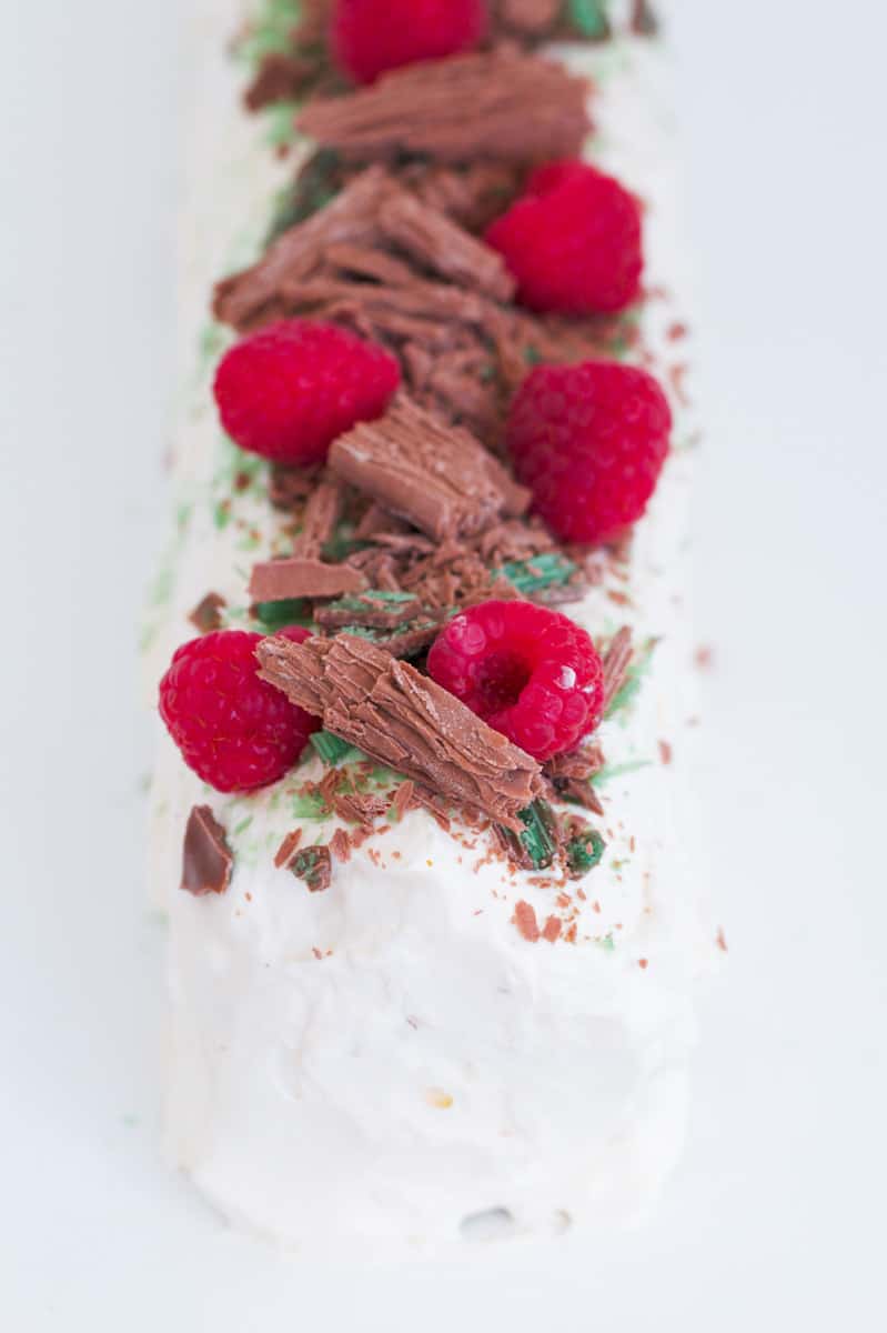 A whipped cream dessert log decorated with raspberries and chocolates.