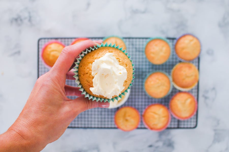 Buttercream being spread onto vanilla cupcakes.