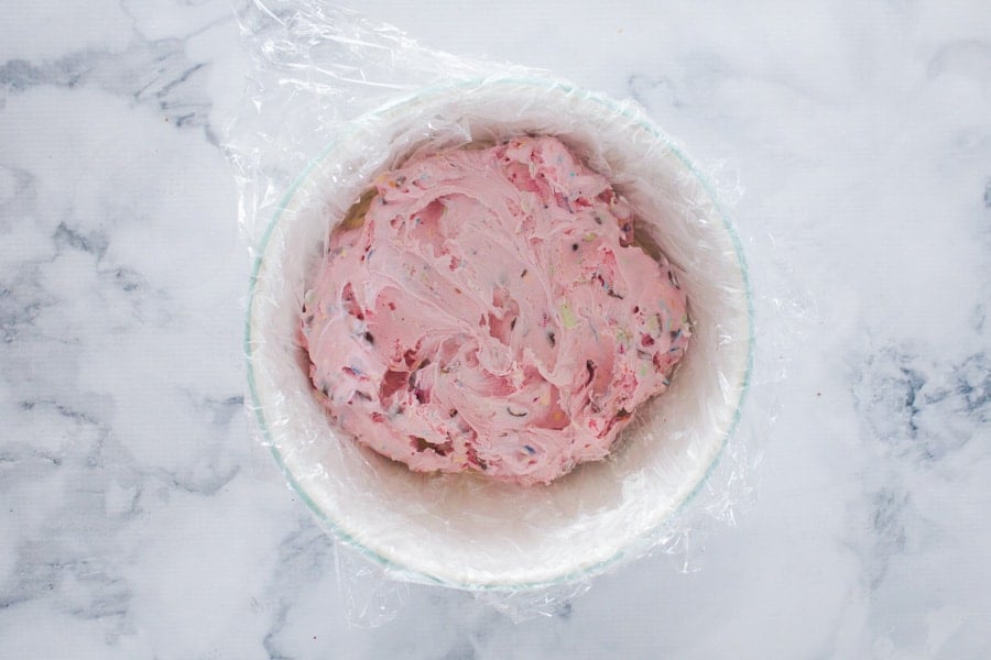 Strawberry ice-cream being pressed into a plastic wrapped bowl. 