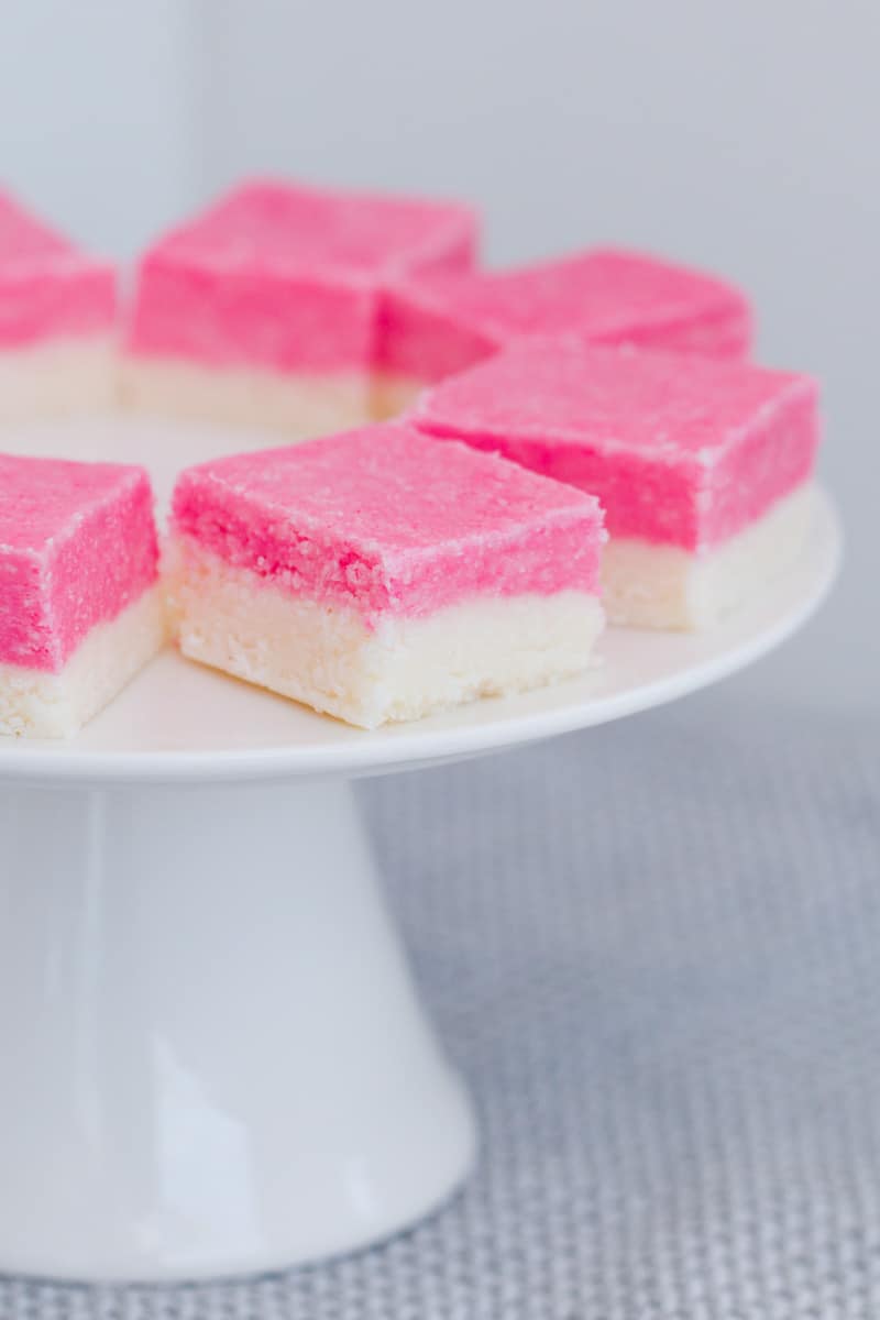Two layered no-bake coconut slice with pink and white on a cake stand.