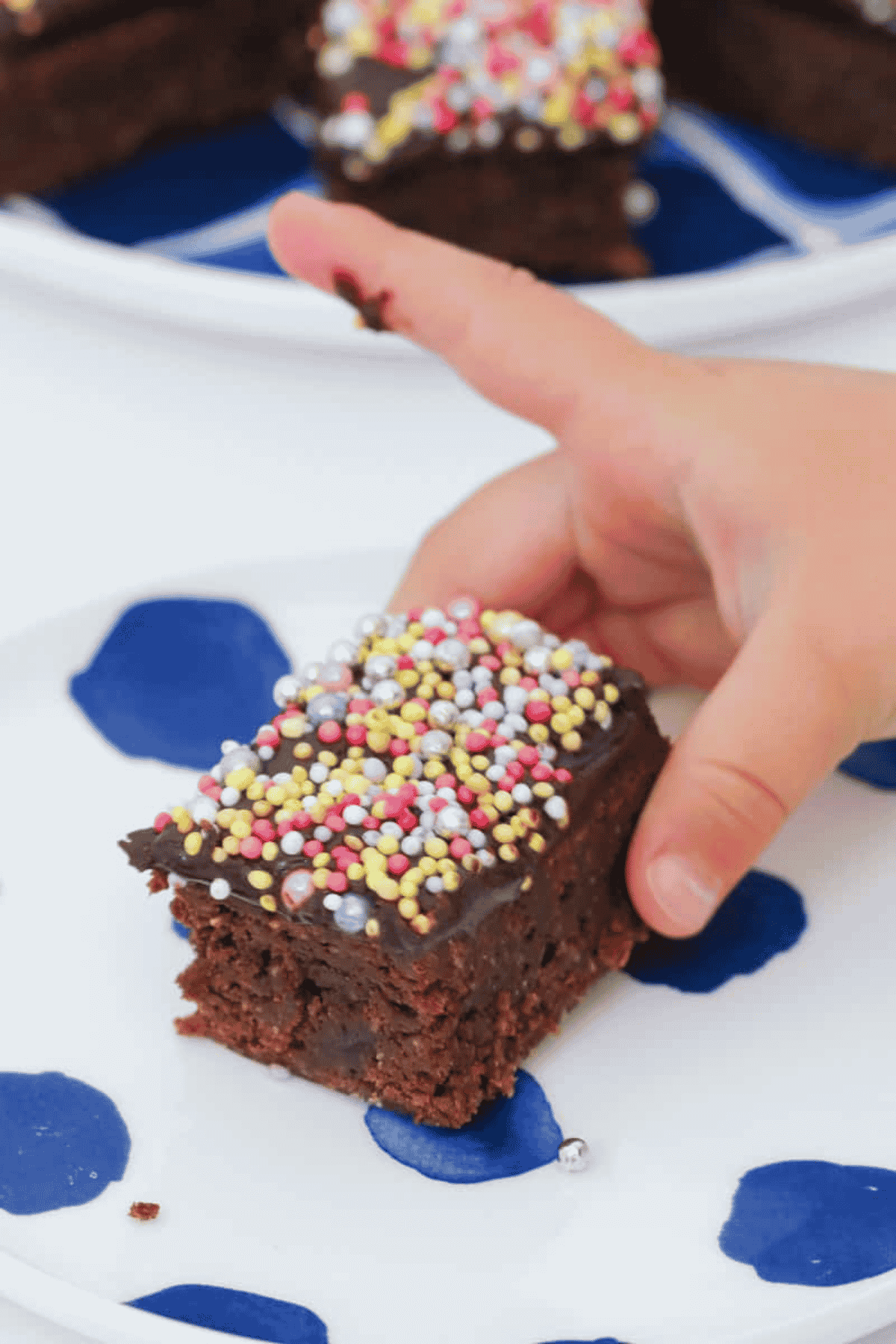 A child's hand holding a piece of sprinkles covered chocolate slice.