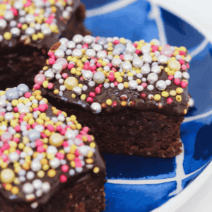 Chocolate slice topped with colorful sprinkles on a blue plate.ing a piece of chocolate slice with sprinkles.